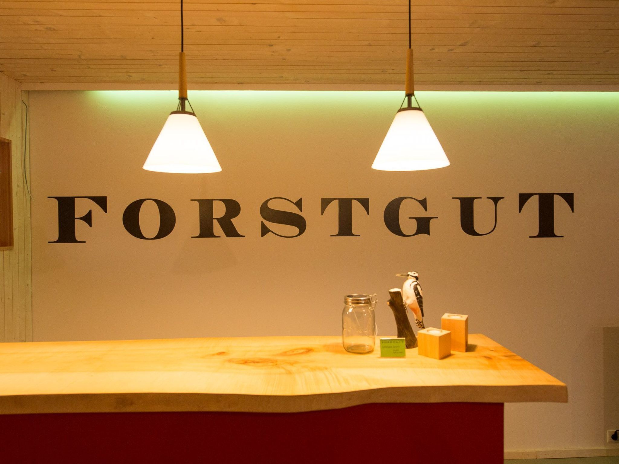 A reception desk with a wooden top and a red base, two pendant lights hanging above, and a wall with the word "FORSTGUT" in large letters.