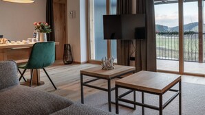 A modern living room with a sofa, a coffee table, a TV mounted on the wall, and a large window with a view of the outdoors. - EXKLUSIVE FERIENWOHNUNG MIT EIGENER SAUNA by Interhome (Regen)