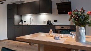 A modern kitchen with dark cabinets, a wooden dining table, and a vase with flowers. - EXKLUSIVE FERIENWOHNUNG MIT EIGENER SAUNA by Interhome (Regen)