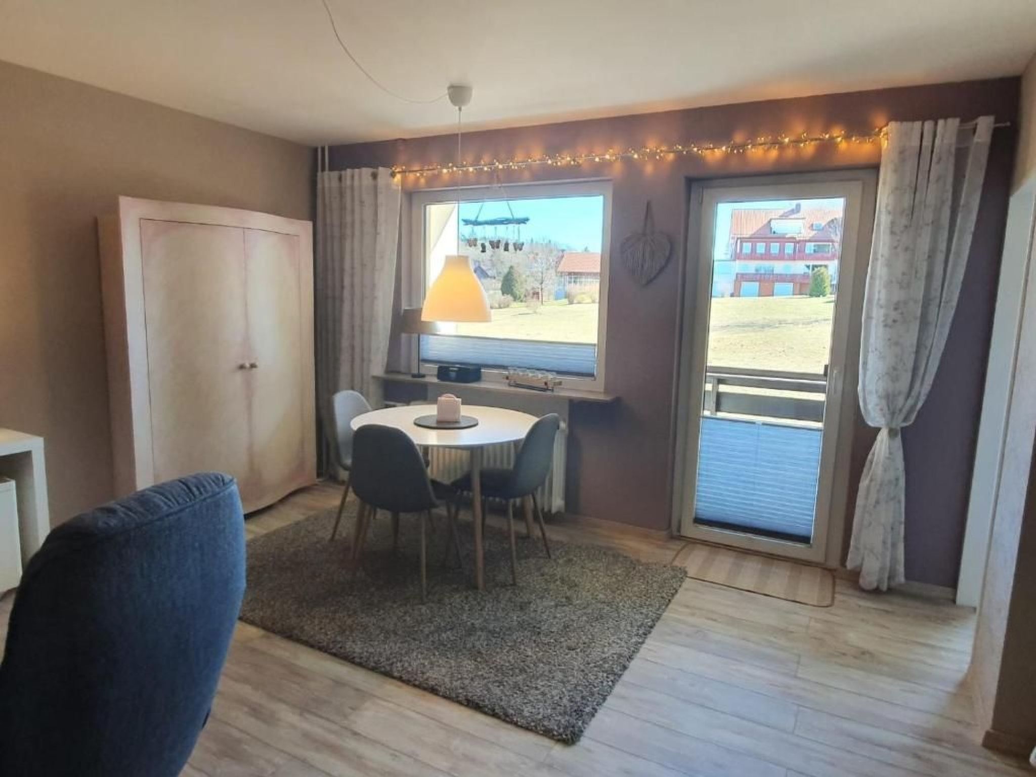 Una habitación pequeña con una mesa redonda, dos sillas, una lámpara y una ventana con cortinas.