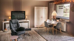 A modern living room with a flat-screen TV, a comfortable armchair, a dining table with chairs, and a large window with curtains. - Harzgeiss by Interhome (Braunlage)