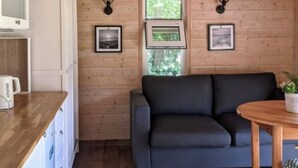 Tunnelmallinen huone, jossa on puuseinät, harmaa sohva, puinen pöytä ja valkoinen kaappi, jonka päällä on vedenkeitin.