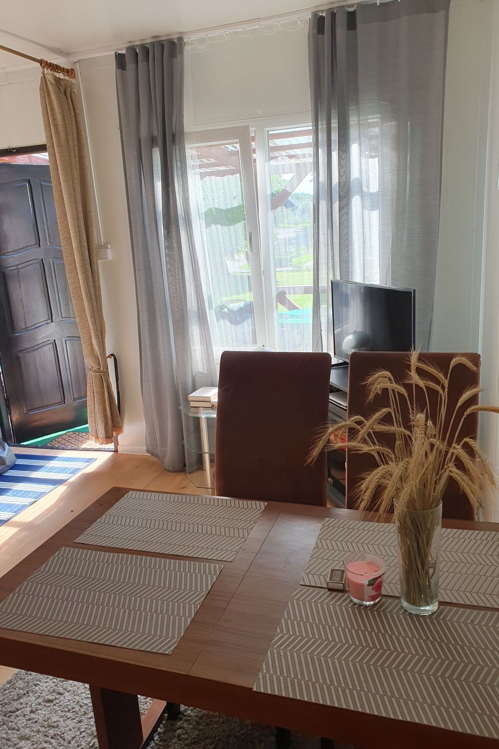 A living room with a wooden table, two chairs, a TV, and a window with curtains.