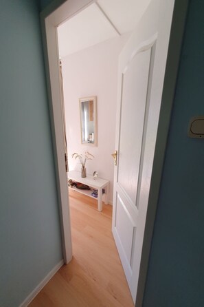 Ein Flur mit einer weißen Tür, einer kleinen weißen Bank und einem Spiegel an der Wand.