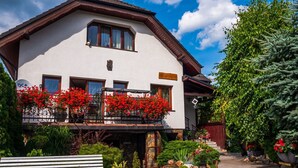 A two-story building with a balcony adorned with red flowers, a stone pathway, and a bench. - Wohnung mit Terrasse, Garten und Grill by Interhome (Myslakowice)