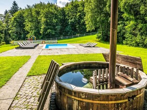 A wooden hot tub surrounded by a stone pathway, a swimming pool, and lounge chairs in a garden setting. - Landhaus mit Schwimmbad by Interhome (Szklarska Poreba)