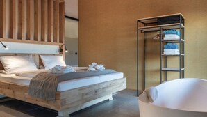 Quarto moderno com cabeceira de madeira, cama grande com roupa de cama branca, estante embutida com toalhas dobradas e banheira branca.
