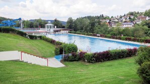 Piscina com torre de salva-vidas, cercada por grama verde e arbustos.