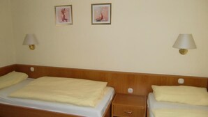 Hotellihuone, jossa on kaksi sänkyä, puinen pääty, yöpöydät lampuineen ja kaksi kehystettyä kuvaa seinällä.