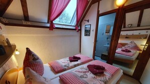 Una stanza accogliente con due letti, ognuno con copriletto a quadretti rossi e cuscini a forma di cuore. Il soffitto è in legno e presenta una finestra con tende rosse.