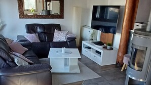 Ein modernes Wohnzimmer mit einem schwarzen Ledersofa, einem weißen Couchtisch, einem Flachbildfernseher, einer weißen Unterhaltungsanlage und einem Kaminofen.