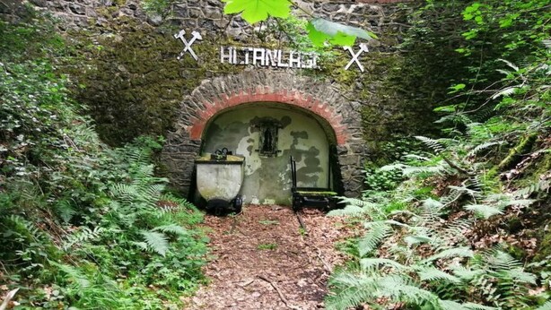 Ein steinerner Bogen, der in einen Tunnel führt, mit einem Schild mit der Aufschrift "HILTLAND" und zwei gekreuzten Schwertern.