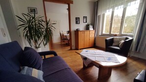 Una sala de estar con un sofá, una mesa de centro, una mesa de comedor con sillas, un aparador y una planta en maceta.