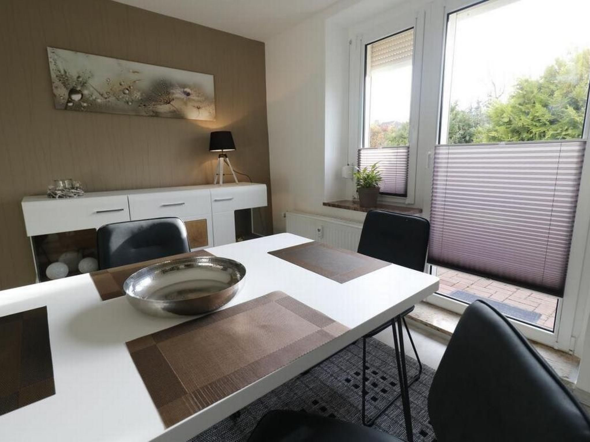 Un comedor moderno con una mesa blanca, individuales marrones y un centro de mesa con un bol de metal.