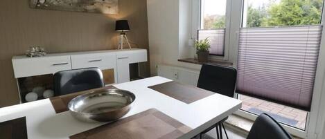 Un comedor moderno con una mesa blanca, individuales marrones y un centro de mesa con un bol de metal.