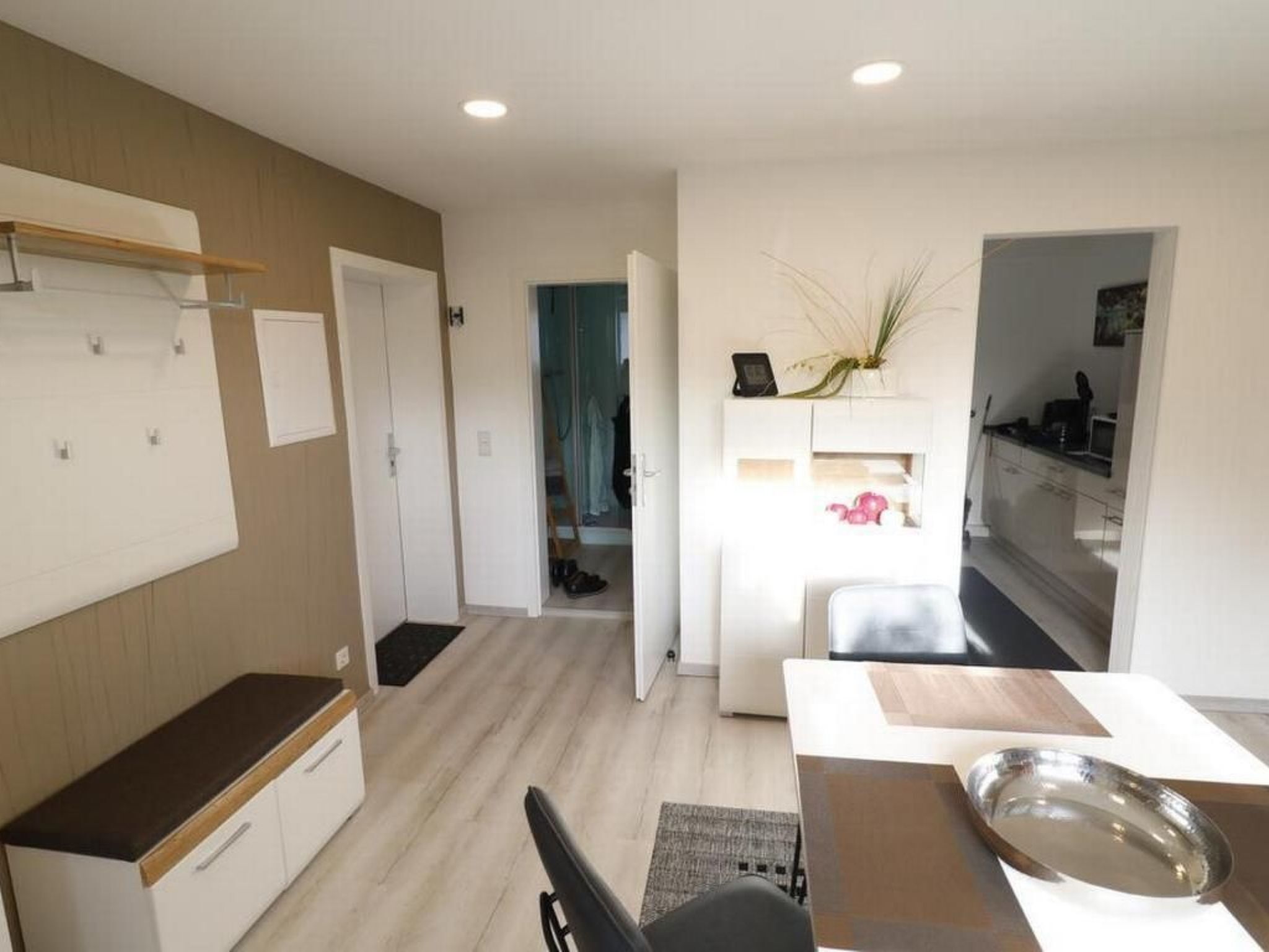 Une cuisine moderne avec des meubles blancs, un plan de travail en bois et un coin repas comprenant une table et des chaises.