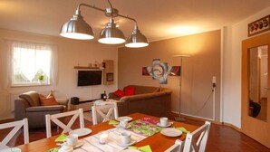 A dining area with a wooden table set for four, surrounded by white chairs. There is a sofa and a television in the background. - Abendsonne by Interhome (Mirow)