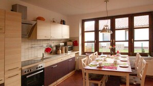 A kitchen with wooden cabinets, a stove, and a dining table set for four. - Abendsonne by Interhome (Mirow)