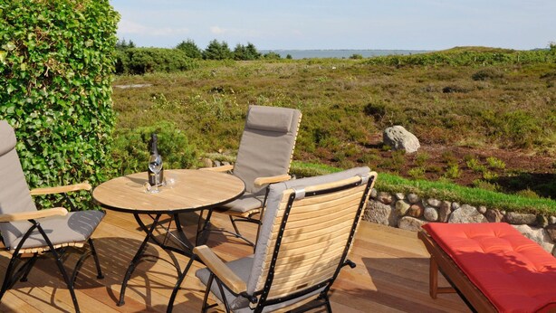 An outdoor seating area with a round wooden table and chairs, a bottle of wine, and a view of a grassy landscape. - Sönshörn - S20 - in Munkmarsch by Interhome (Archsum)