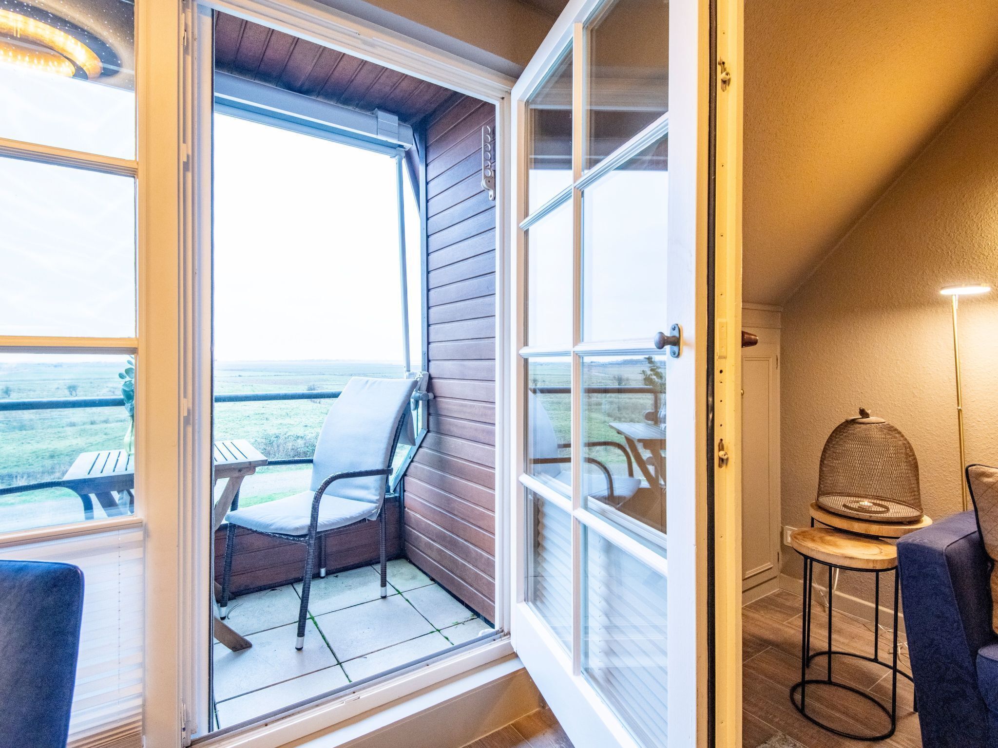 Un balcon avec un fauteuil en osier, une petite table et une lampe.