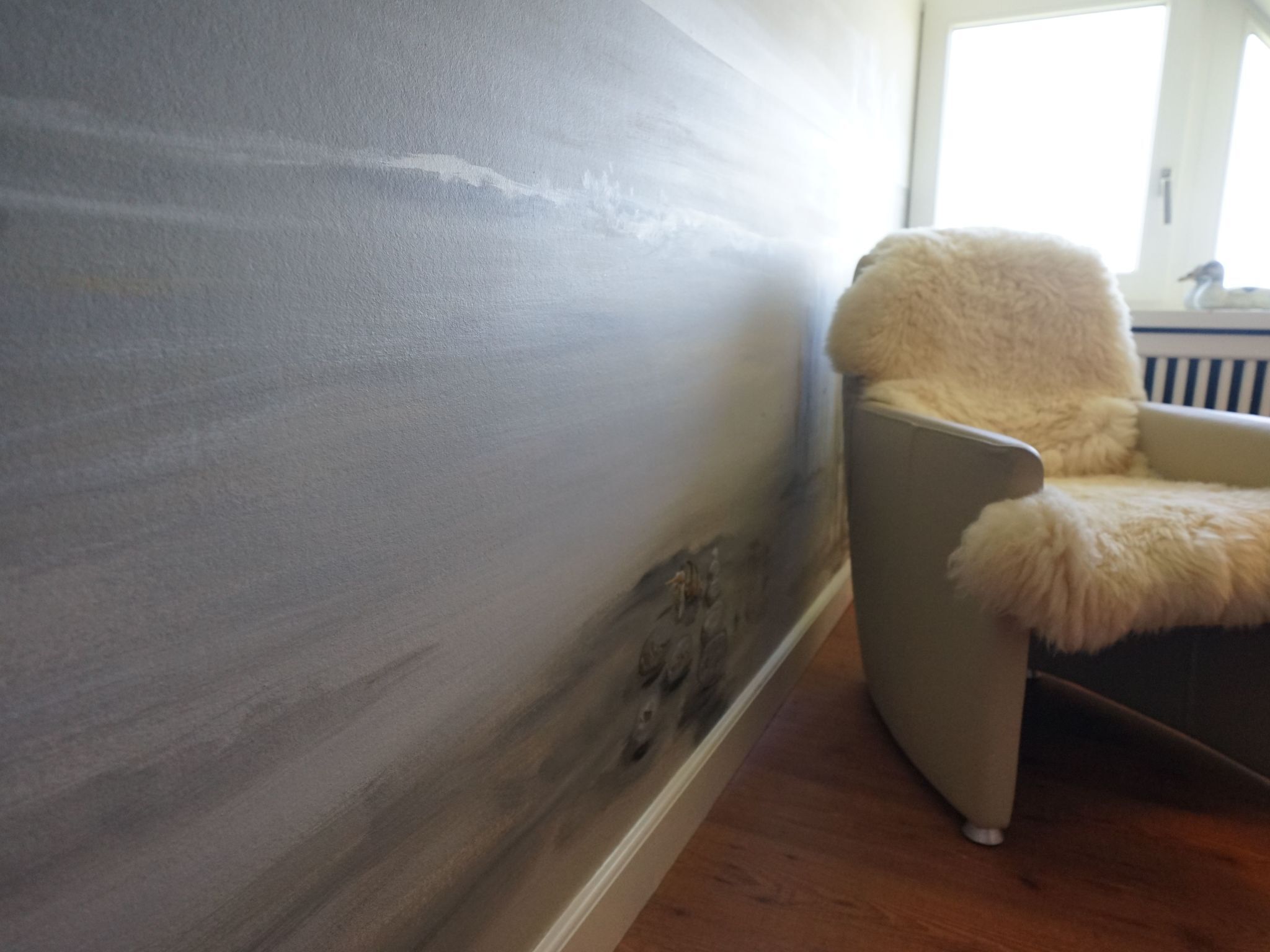 A room with a grey textured wall, a fluffy white chair, and a window with a view of a building.