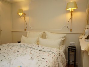 Een hotelkamer met een groot bed, twee wandlampen, een nachtkastje met een lamp en een klein nachtkastje.