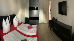 Habitación de hotel con dos camas, un escritorio, una silla, un televisor montado en la pared y un armario.