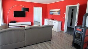 Una sala de estar moderna con un sofá gris, un televisor de pantalla plana montado en una pared roja, un mueble blanco para equipos electrónicos y una chimenea.