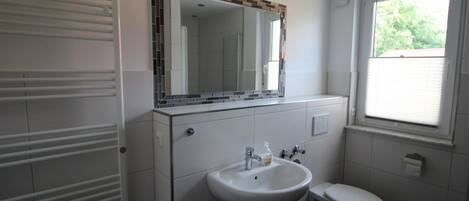 Une salle de bain moderne avec un lavabo blanc, des toilettes et une fenêtre.