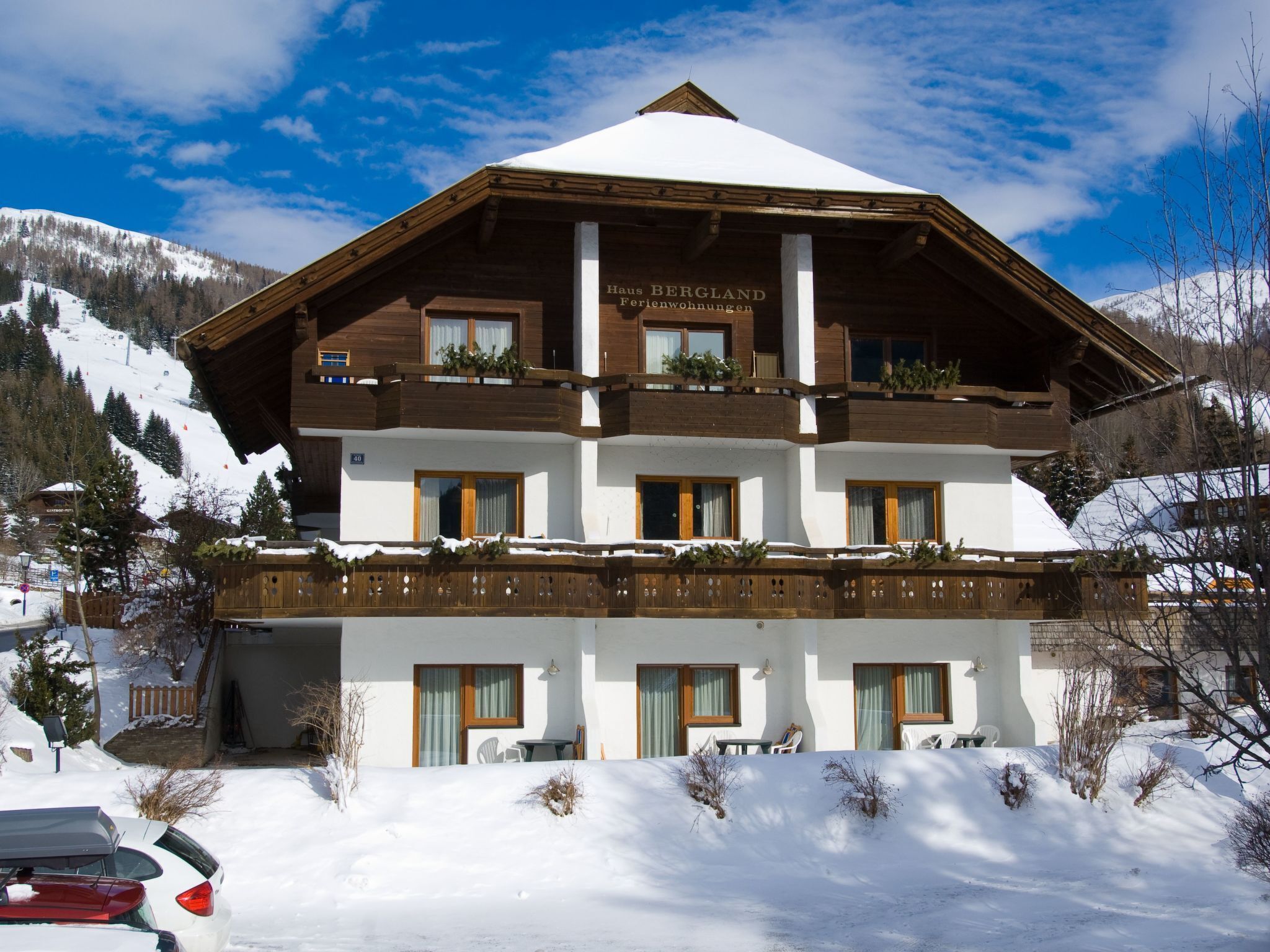 A multi-story chalet with a snow-covered roof, wooden balconies, and a view of a snowy mountain.