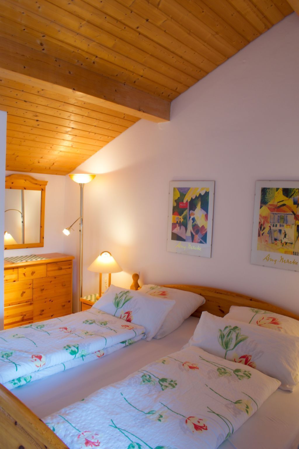 A bedroom with two beds, wooden ceiling, a dresser, a mirror, and two wall-mounted lamps.