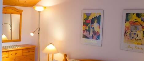 A bedroom with two beds, wooden ceiling, a dresser, a mirror, and two wall-mounted lamps.