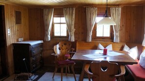 Interior de una cabaña de madera con una mesa de comedor, sillas, un banco y un aparador.