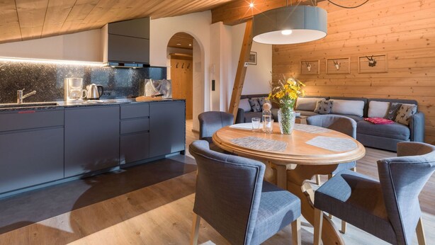 Una cucina moderna con mobili scuri, soffitto in legno e zona pranzo con un tavolo rotondo e sedie.