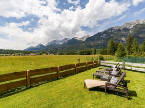 Eine begrünte Außenanlage mit Holzzaun, Picknicktisch und Liegestühlen.