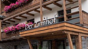 Ein Gebäude mit einem Schild, auf dem 'Der Zirmhof' steht, und einem Balkon mit rosa Blüten.