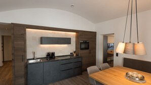 Eine moderne Küche mit dunklen Schränken, einem eingebauten Ofen und einer großen Kochinsel mit Spüle. Es gibt einen Essbereich mit Holztisch und Stühlen.
