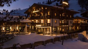 Ein mehrstöckiges Hotel mit beleuchteter Beschilderung, einer schneebedeckten Fassade und einem Bergpanorama im Hintergrund.