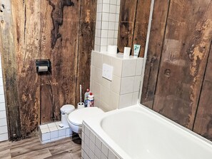 Een badkamer met een houten wand, een wit bad, een toilet en een handdroger.