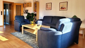 Ein Wohnzimmer mit Holzboden, zwei blauen Sofas, einem Couchtisch und einem Bücherregal.