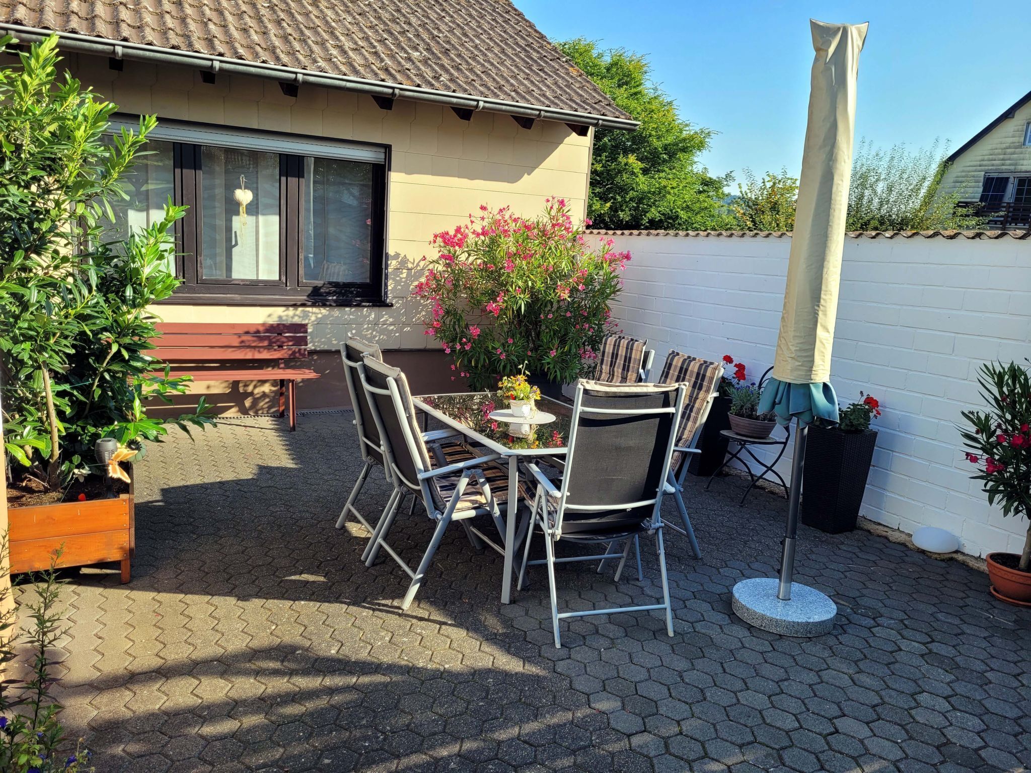 Une terrasse extérieure avec une table et des chaises, entourée de plantes en pot et d’un mur blanc.