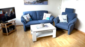 A living room with a blue sofa, a white coffee table, and a TV on a wooden stand. - Martina by Interhome (Friederikensiel)