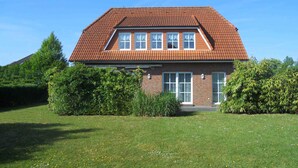A two-story house with a red-tiled roof, brick walls, and a front yard with grass and bushes. - Martina by Interhome (Friederikensiel)