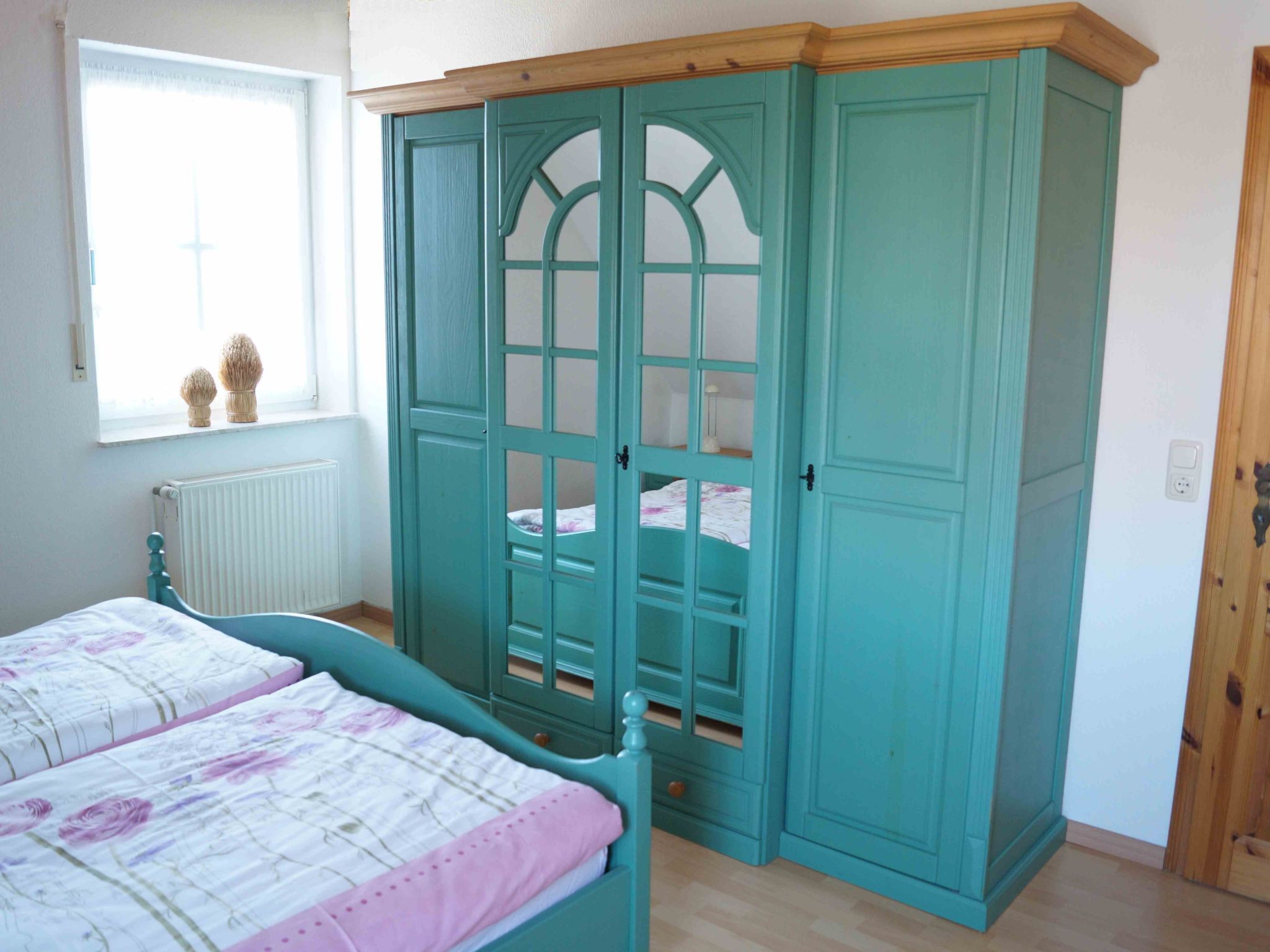 Ein Schlafzimmer mit einem Bett, einem Fenster und einem türkisblauen Kleiderschrank.