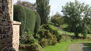 A stone building with a well-maintained hedge and a cobblestone path leading to a grassy area with trees. - Ruhiges Landhaus mit zwei gemütlichen Wohnungen by Interhome (Bereborn)