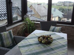 Un rinc ón acogedor con una mesa, una planta en maceta y vistas a casas a través de amplios ventanales.