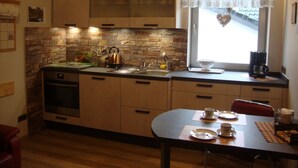 A compact kitchen with a stone backsplash, a kettle, a coffee maker, and a dining area with a table set for two. - Ruhiges Landhaus mit zwei gemütlichen Wohnungen by Interhome (Bereborn)