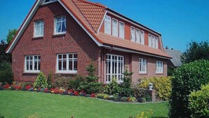 A two-story brick house with a gabled roof, multiple windows, and a well-maintained garden with various plants and flowers. - Strandnah Ilse Hans by Interhome (Friederikensiel)