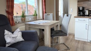 A cozy living area with a sofa, a small table, and a kitchen area with a coffee maker. - Strandnah Ilse Hans by Interhome (Friederikensiel)