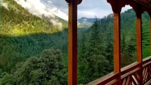 Un balcón de madera con vistas a una cadena montañosa boscosa.